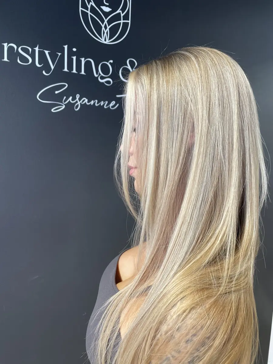 Langes, glatt fallendes Blond mit weichem Ansatzverlauf vor der Salonwand